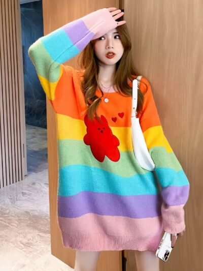 woman posing in cue colorful sweater, she has one hand up and she has a white bag over the other one