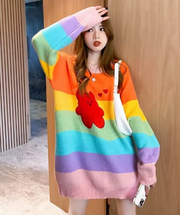 woman posing in cue colorful sweater, she has one hand up and she has a white bag over the other one