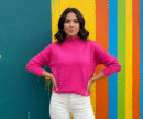 woman with dark brown short hair wearing fushcia sweater and white pants in a colorful room, she is smiling gently