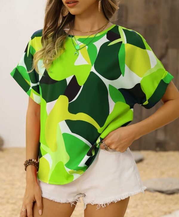 woman standing in green colorful blouse and putting her hand into a pocket of white shorts