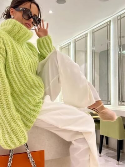 woman wearing green colorful turtleneck sweater, white pants and holding an orange bag