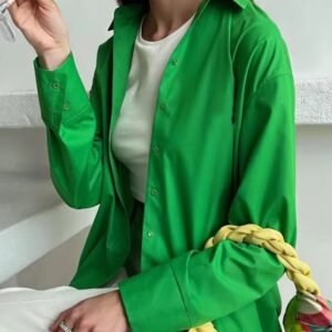 woman wearing green oversized colorful blouse and drinking orange juice