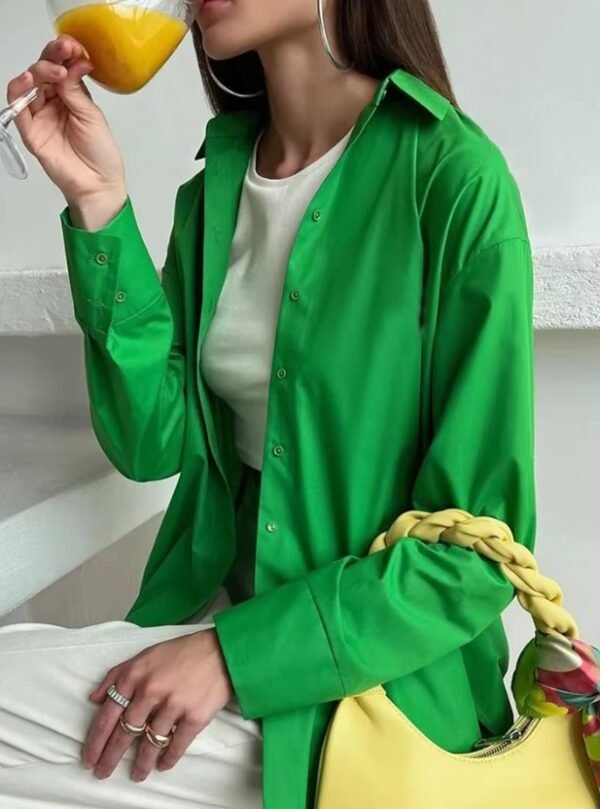 woman wearing green oversized colorful blouse and drinking orange juice