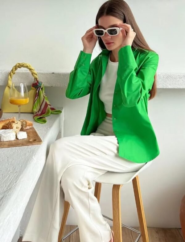 woman wearing green oversized colorful blouse and white pants, she is sitting at the white table