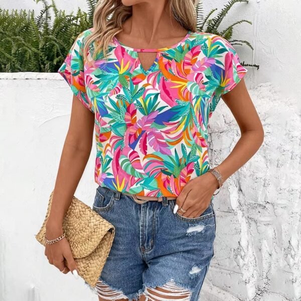 woman wearing Hawaiian colorful blouse, jeans shorts and a small beige purse, white wall behind her