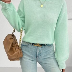 woman wearing mint sweater, jeans and a silver necklace, she is holding a brown purse.