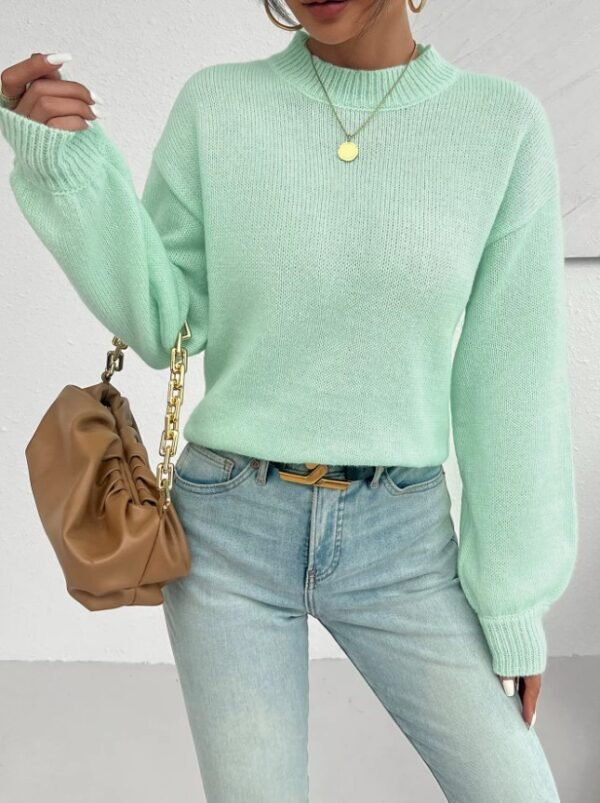 woman wearing mint sweater, jeans and a silver necklace, she is holding a brown purse.