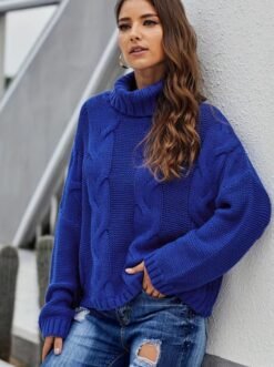 woman with brown hair wearing navy blue colorful sweater and jeans, grey building behind her