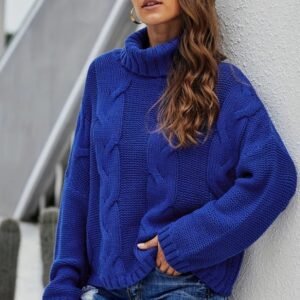 woman with brown hair wearing navy blue colorful sweater and jeans, grey building behind her