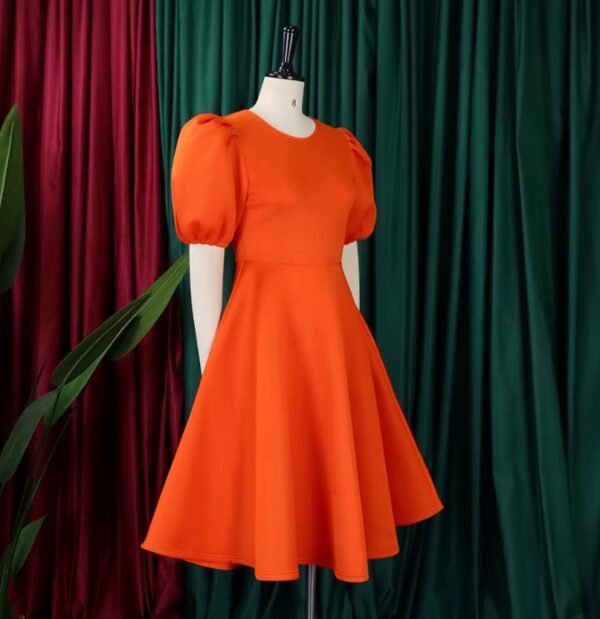 side view of orange dress on a mannequin, red and green curtains in the background