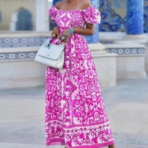 woman wearing pink colorful bohemian dress and carrying a white bag, blue and grey concrete behind her