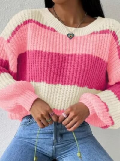 woman wearing pink colorful sweater and jeans, white wall behind her