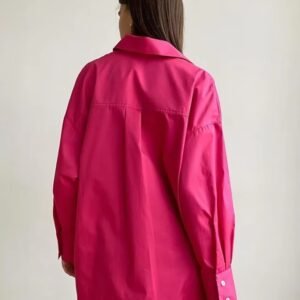 woman turned to her back wearing pink oversized colorful blouse, white wall behind her