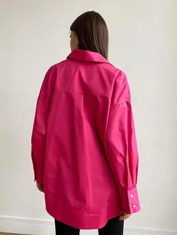 woman turned to her back wearing pink oversized colorful blouse, white wall behind her