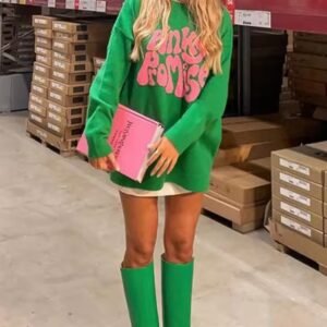 woman with blonde hair wearing colorful pinky promise sweater and long green boots, she is holding a pink book