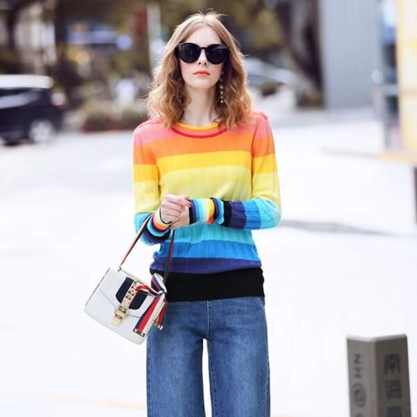 woman wearing rainbow sweater and jeans, she is holding an elegant purse, street in the background