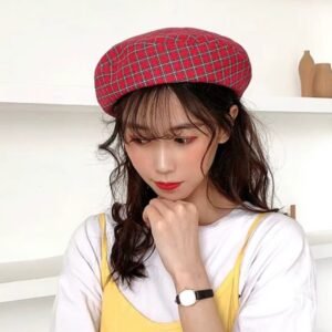 woman wearing red plaid colorful beret and a white T-shirt, white wall behind her