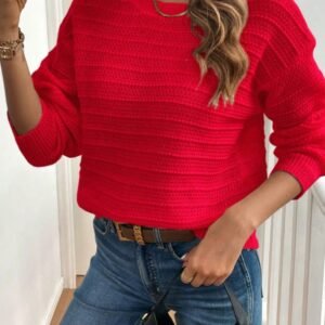 woman wearing red sweater and jeans, she is holding her phone in one hand and a black bag in the other