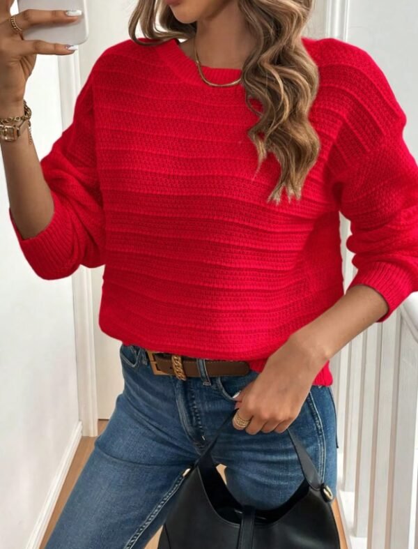 woman wearing red sweater and jeans, she is holding her phone in one hand and a black bag in the other