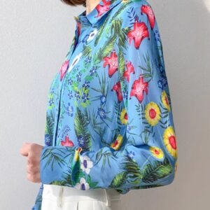 woman turned to her side wearing silk colorful blouse, white wall behind her