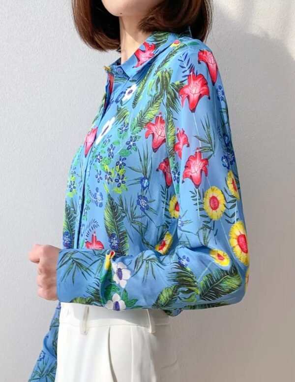 woman turned to her side wearing silk colorful blouse, white wall behind her