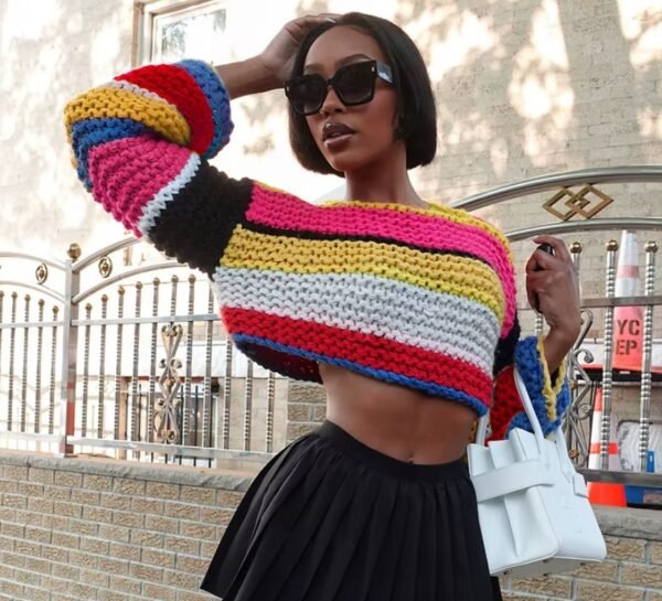 woman wearing stylish colorful sweater, black short skirt and holding a white bag, the street behind her