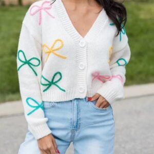 woman with black hair wearing buttoned sweet colorful cardigan and bright jeans, grass in the backgorund