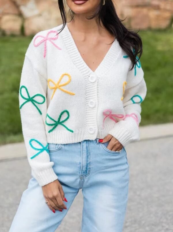 woman with black hair wearing buttoned sweet colorful cardigan and bright jeans, grass in the backgorund