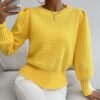 woman wearing yellow sweater and white jeans, she is holding her phone and sitting on a white sofa