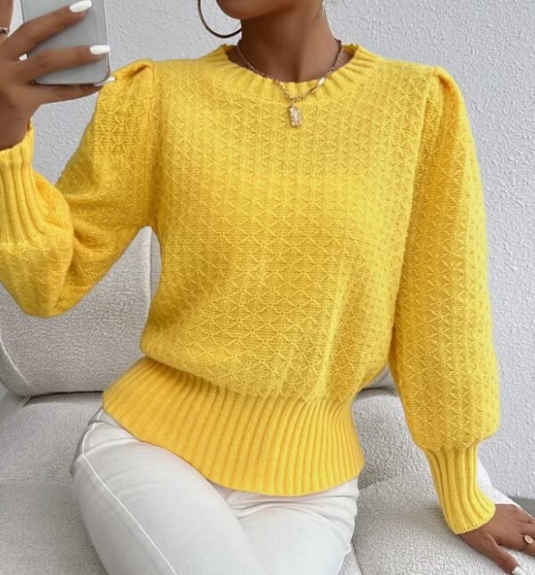 woman wearing yellow sweater and white jeans, she is holding her phone and sitting on a white sofa