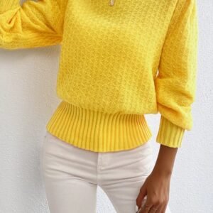 woman wearing yellow sweater and white jeans, she is holding a gold bag, white wall behind her