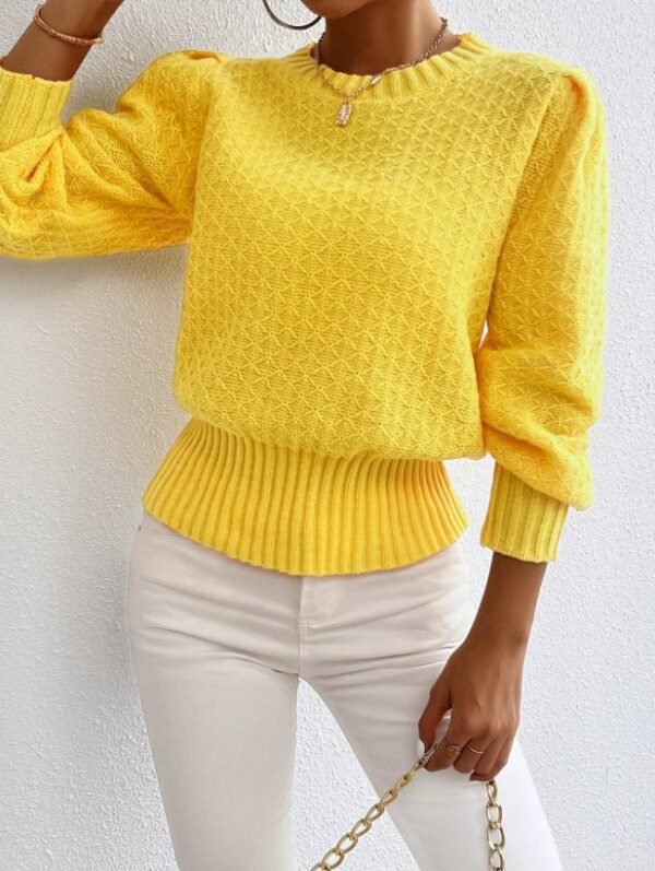 woman wearing yellow sweater and white jeans, she is holding a gold bag, white wall behind her