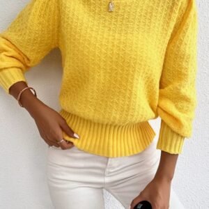 woman wearing yellow sweater, white jeans and a silver necklace, she is leaning over a white wall