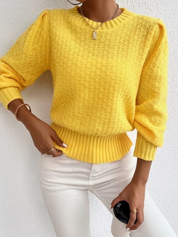 woman wearing yellow sweater, white jeans and a silver necklace, she is leaning over a white wall