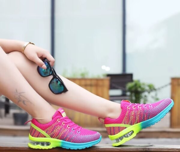 woman with a tattoo on her lag wearing athletic colorful sneakers and holding black sunglasses, window in the background