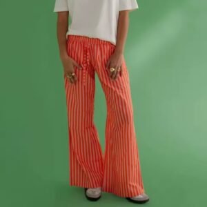 woman wearing orange colorful baggy pants and a white shirt, green background