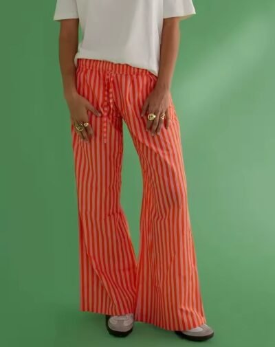 woman wearing orange colorful baggy pants and a white shirt, green background