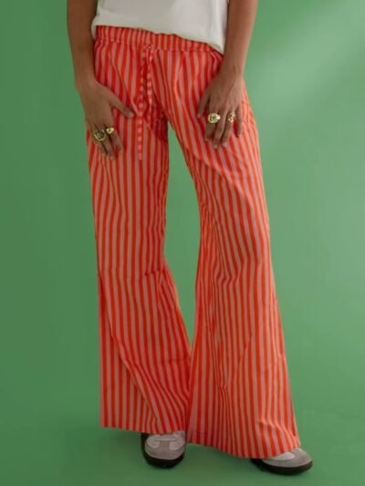 woman wearing orange colorful baggy pants and a white shirt, green background