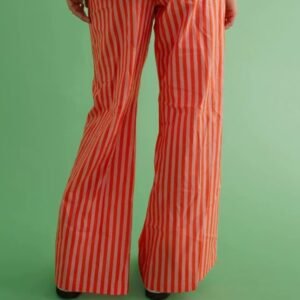 woman turned to her back wearing orange colorful baggy pants and a white shirt, green background