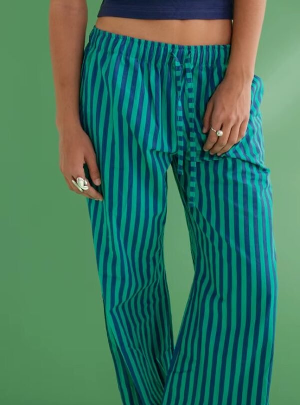 woman wearing blue colorful baggy pants and a black top, green background