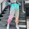 woman wearing colorful cargo pants, white top and white sneakers, grey stairs behind her