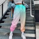 woman wearing colorful cargo pants, white top and white sneakers, grey stairs behind her