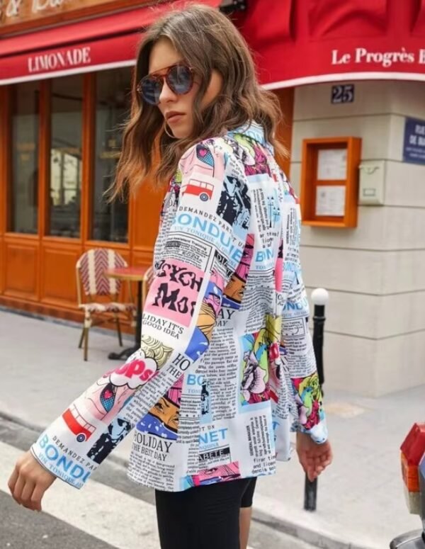 woman turned to her back wearing colorful newspaper blazer and black shorts, red and grey building behind her