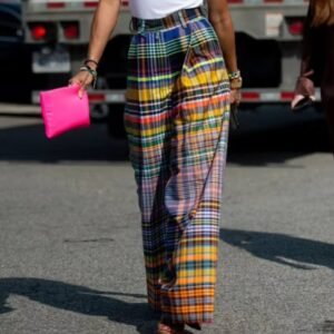 woman wearing colorful plaid pants and black high heels, she is carrying a hot pink purse, a grey street in the background