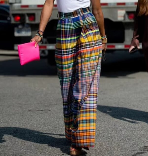 woman wearing colorful plaid pants and black high heels, she is carrying a hot pink purse, a grey street in the background