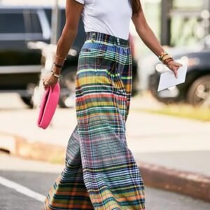 woman wearing colorful plaid pants and a white top, she is carrying a piece of paper and pink purse, a street in the background