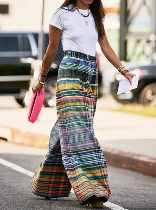 woman wearing colorful plaid pants and a white top, she is carrying a piece of paper and pink purse, a street in the background