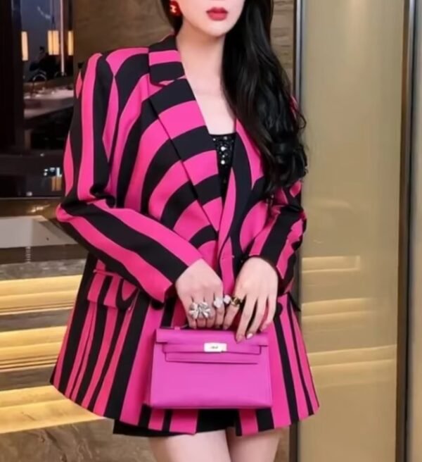 woman wearing colorful striped blazer and lifting a pink purse up