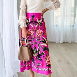 woman wearing colorful tropical skirt and a white top, she is holding a beige bag, bright room behind her