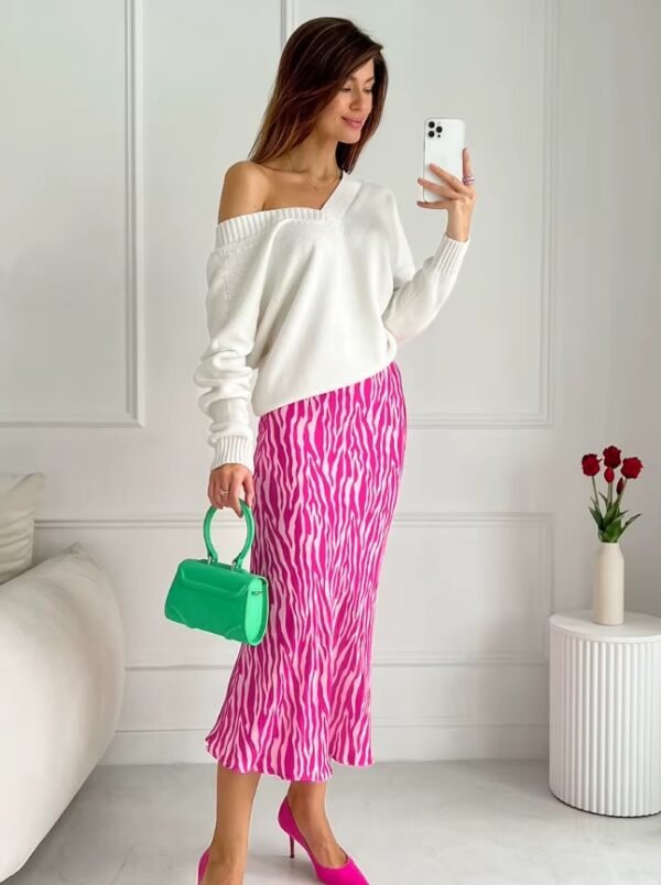 woman with brown hair wearing colorful zebra skirt, white top and carrying a green purse, white room and red flowers behind her